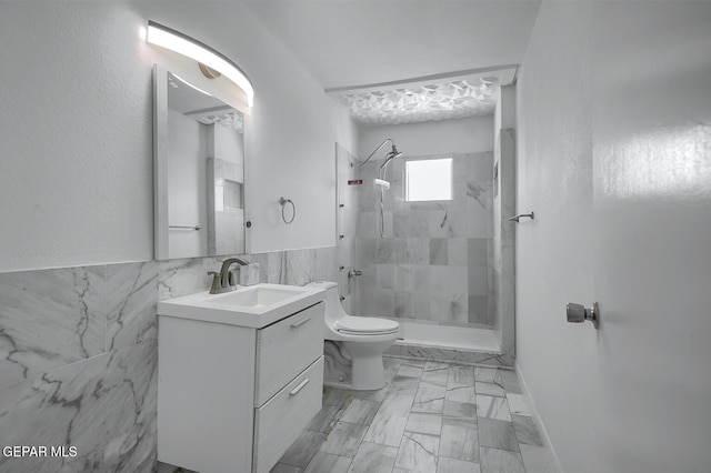 full bathroom featuring tile walls, toilet, tiled shower, marble finish floor, and vanity