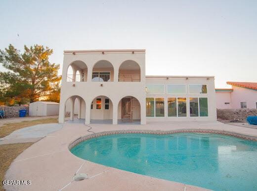 back of house featuring a balcony, an outdoor pool, a patio, and stucco siding