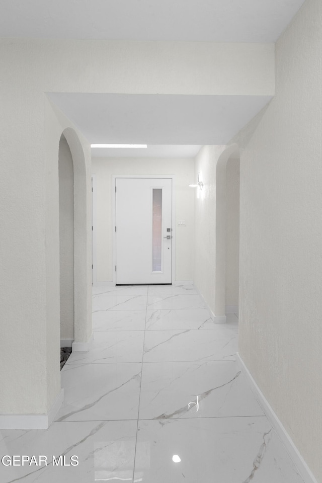 corridor featuring arched walkways, marble finish floor, and baseboards