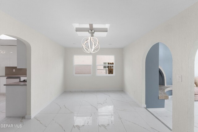 spare room featuring baseboards, arched walkways, marble finish floor, and an inviting chandelier