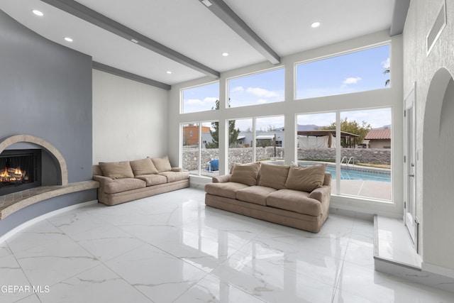 living room featuring beam ceiling, recessed lighting, a warm lit fireplace, a high ceiling, and marble finish floor