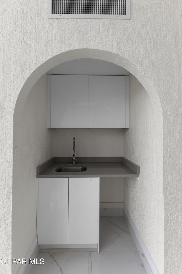 kitchen featuring baseboards, visible vents, marble finish floor, and a sink