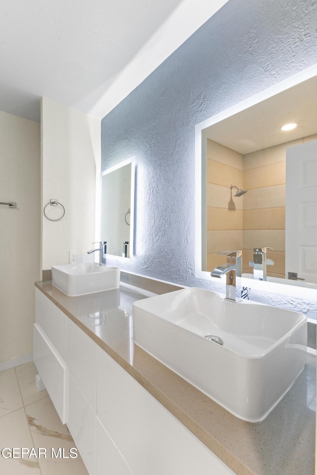 full bathroom with double vanity, a shower, a textured wall, and a sink