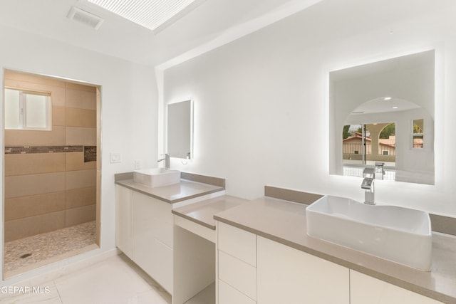 bathroom featuring two vanities, tiled shower, visible vents, and a sink