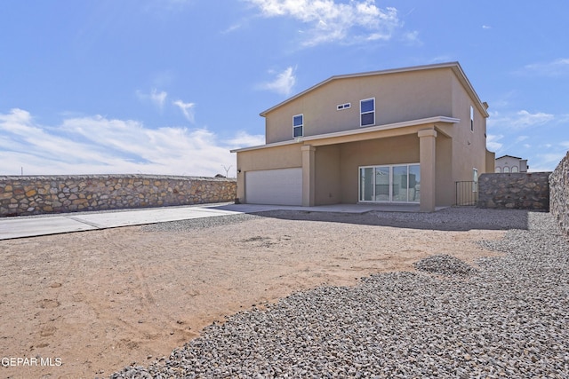 back of house with fence, a garage, driveway, and stucco siding