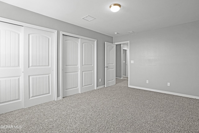 unfurnished bedroom featuring two closets, visible vents, baseboards, and carpet floors