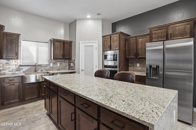 kitchen featuring a sink, dark brown cabinets, appliances with stainless steel finishes, backsplash, and a center island