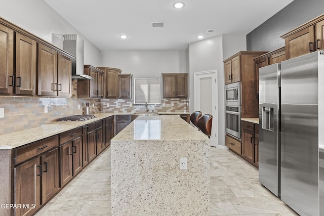 kitchen featuring visible vents, a sink, a center island, appliances with stainless steel finishes, and wall chimney range hood