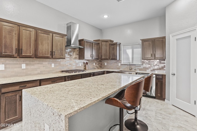 kitchen with a kitchen island, wall chimney range hood, appliances with stainless steel finishes, marble finish floor, and a sink