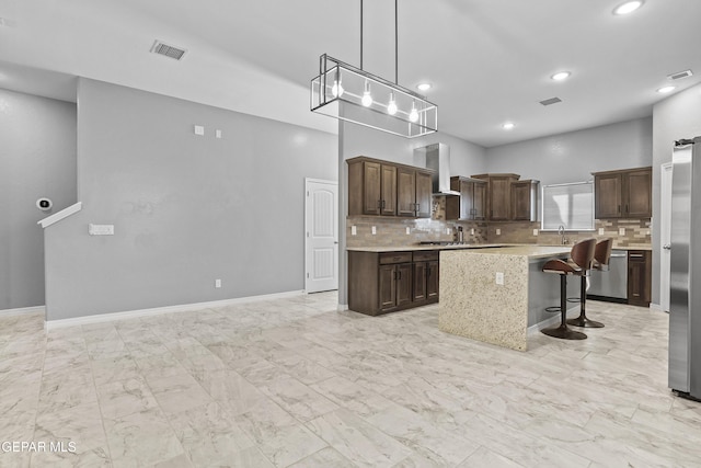 kitchen with backsplash, a kitchen island, dark brown cabinetry, wall chimney range hood, and light countertops