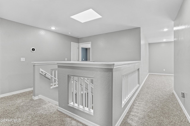 hall with an upstairs landing, carpet flooring, a skylight, and baseboards