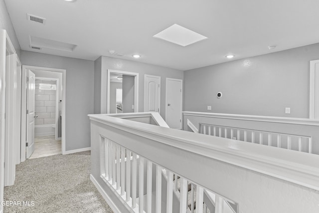 corridor with visible vents, an upstairs landing, light colored carpet, and a skylight