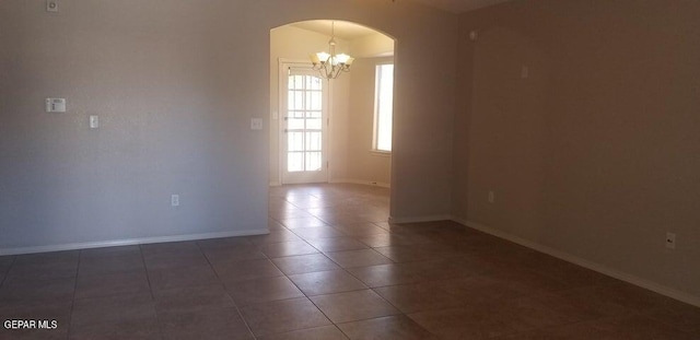 tiled spare room with arched walkways, baseboards, and an inviting chandelier