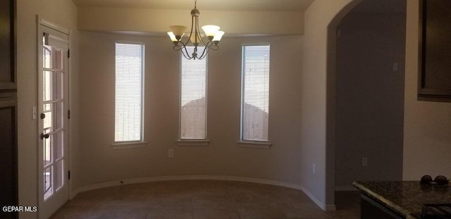 unfurnished dining area with tile patterned floors, baseboards, arched walkways, and a chandelier