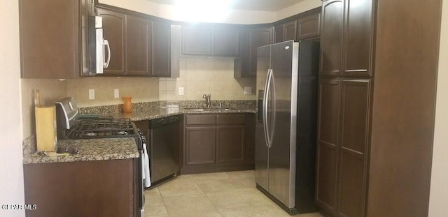 kitchen featuring a sink, backsplash, stainless steel appliances, dark stone counters, and light tile patterned floors