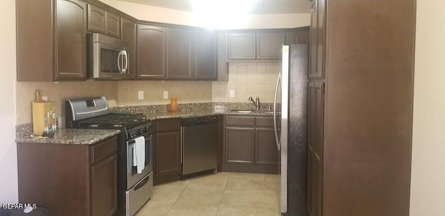 kitchen with stone counters, decorative backsplash, light tile patterned flooring, stainless steel appliances, and a sink