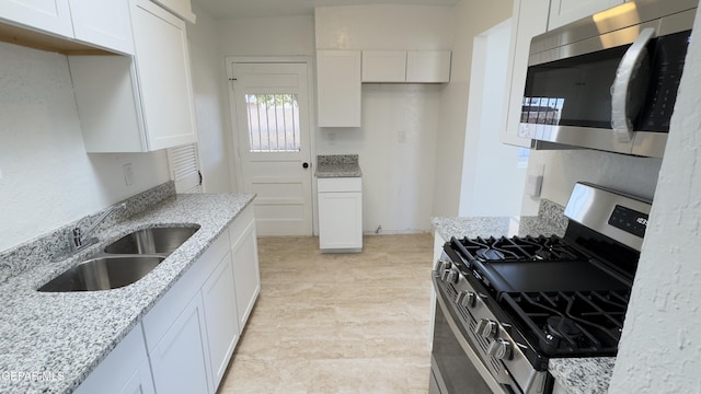 kitchen with white cabinets, light stone counters, appliances with stainless steel finishes, and a sink