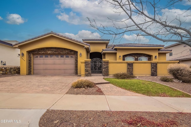 mediterranean / spanish home featuring a fenced front yard, stucco siding, a garage, stone siding, and a gate