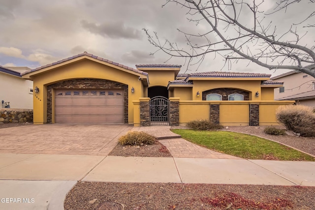 mediterranean / spanish house with a fenced front yard, stucco siding, decorative driveway, a garage, and a gate