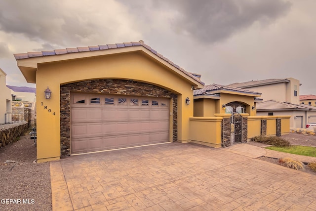 mediterranean / spanish home with stucco siding, decorative driveway, stone siding, fence, and an attached garage