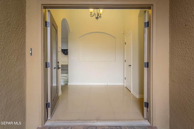 hall featuring tile patterned floors, arched walkways, baseboards, and a textured wall