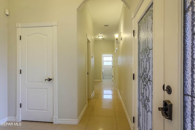 hall featuring light tile patterned floors, arched walkways, and baseboards