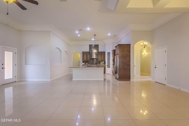 interior space featuring open floor plan, freestanding refrigerator, light tile patterned flooring, arched walkways, and wall chimney exhaust hood