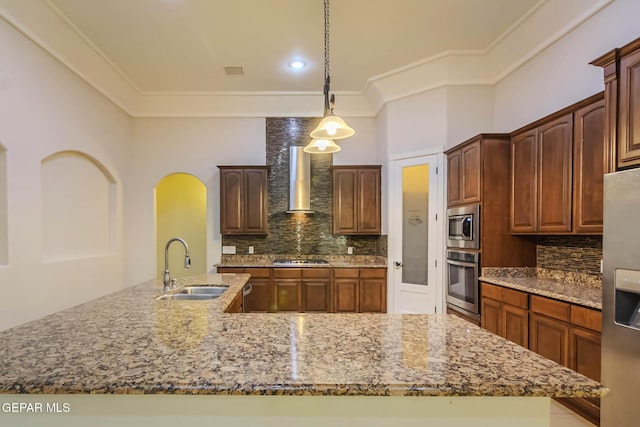 kitchen featuring light stone countertops, a sink, appliances with stainless steel finishes, wall chimney range hood, and tasteful backsplash