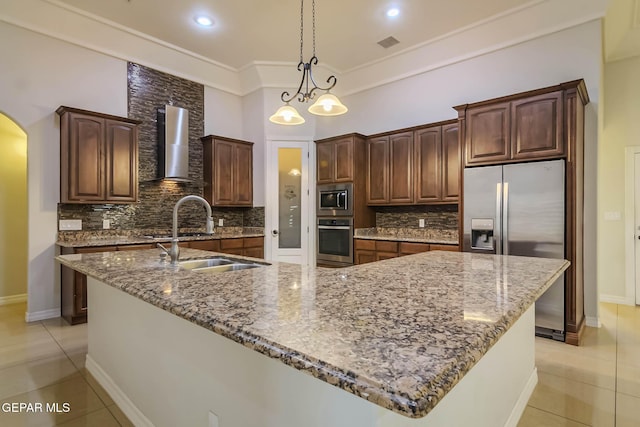 kitchen featuring a sink, arched walkways, appliances with stainless steel finishes, wall chimney range hood, and light tile patterned floors