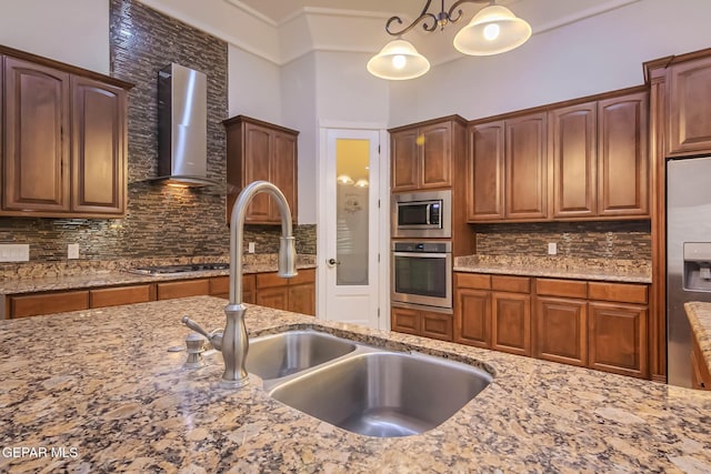 kitchen with a sink, light stone counters, backsplash, stainless steel appliances, and wall chimney range hood