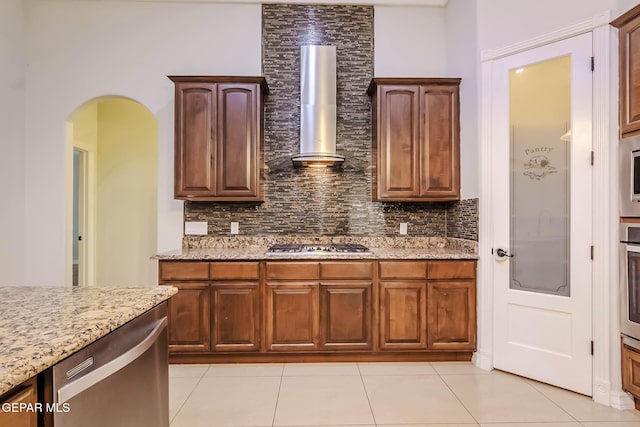 kitchen featuring light stone counters, arched walkways, tasteful backsplash, and wall chimney exhaust hood