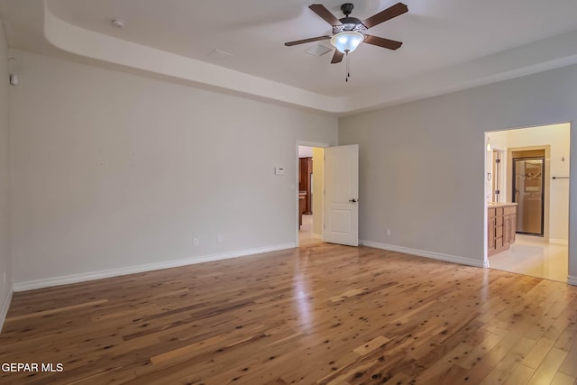 unfurnished room with a tray ceiling, light wood-style floors, baseboards, and ceiling fan