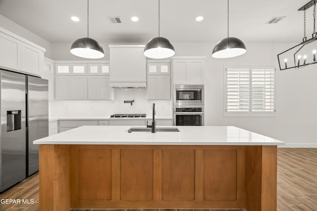 kitchen featuring premium range hood, visible vents, a sink, appliances with stainless steel finishes, and light wood finished floors