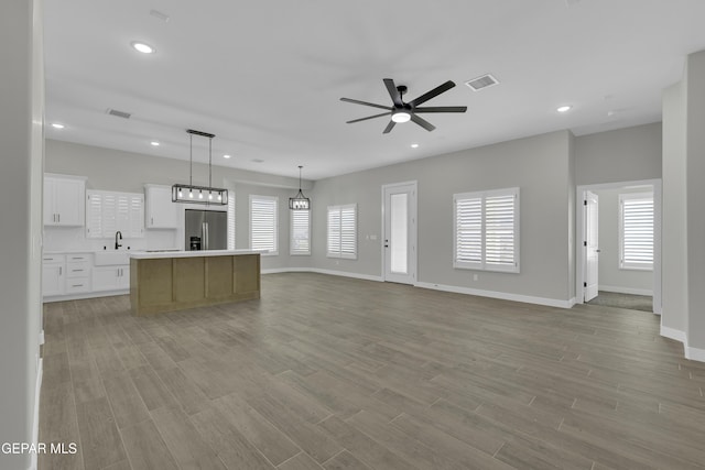 unfurnished living room featuring a wealth of natural light, ceiling fan, a sink, and light wood finished floors