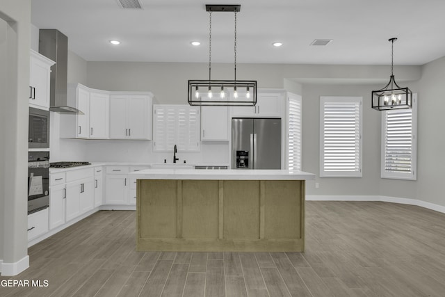 kitchen featuring visible vents, a sink, a kitchen island, stainless steel appliances, and wall chimney exhaust hood