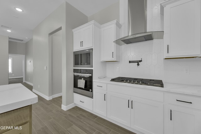 kitchen with backsplash, wood finish floors, appliances with stainless steel finishes, white cabinets, and wall chimney exhaust hood