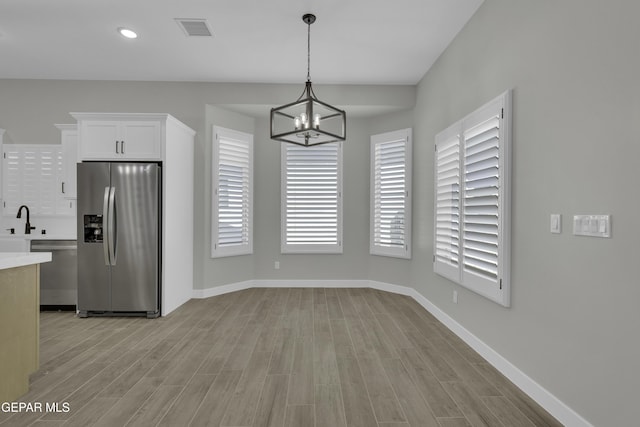 unfurnished dining area with light wood finished floors, visible vents, baseboards, and a sink