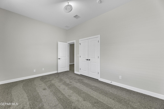 unfurnished bedroom featuring a closet, visible vents, dark carpet, and baseboards