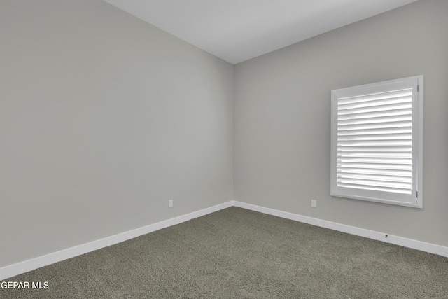 spare room with baseboards and dark carpet