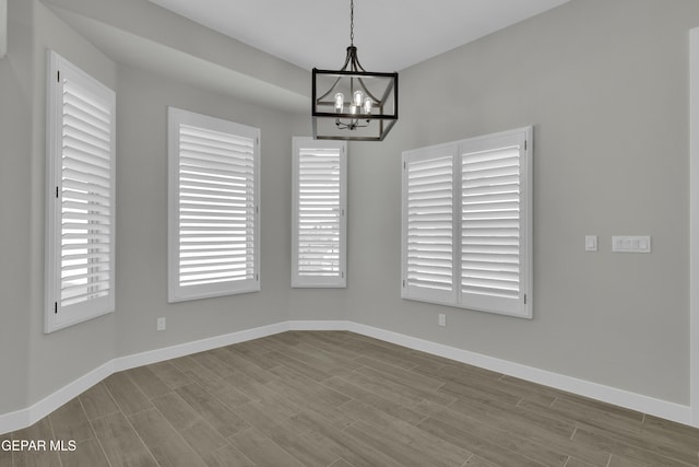 unfurnished dining area with wood finished floors, baseboards, and a chandelier