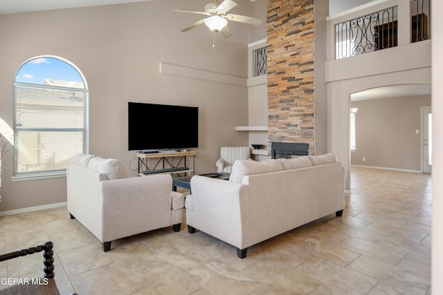 living area with a stone fireplace, baseboards, arched walkways, and ceiling fan