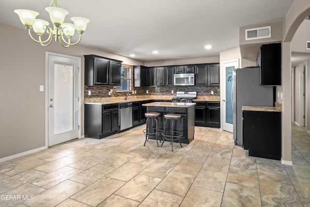 kitchen with visible vents, a kitchen island, decorative backsplash, appliances with stainless steel finishes, and dark cabinetry