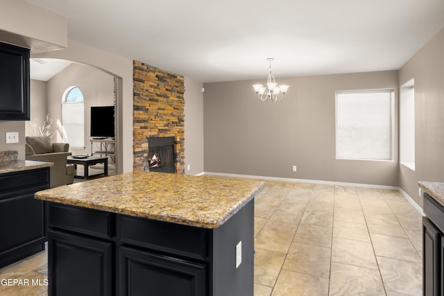 kitchen featuring a kitchen island, dark cabinetry, a stone fireplace, light tile patterned floors, and baseboards