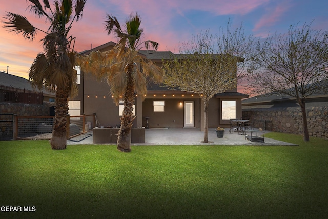 rear view of house with stucco siding, fence, a lawn, and a patio area