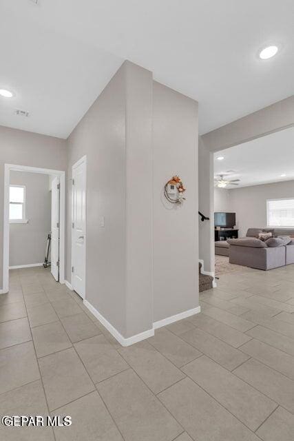 corridor featuring light tile patterned floors, plenty of natural light, stairs, and baseboards