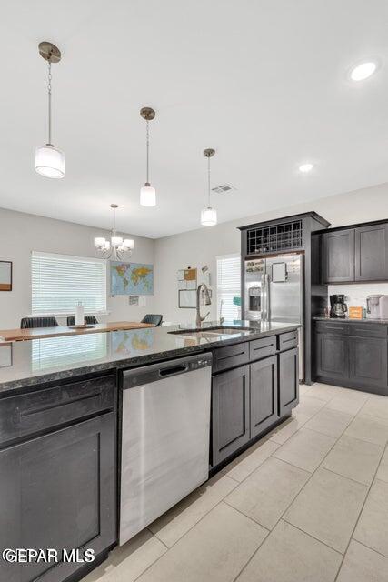 kitchen with a sink, dark stone countertops, hanging light fixtures, and stainless steel appliances