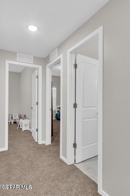 hallway with visible vents, baseboards, and light colored carpet