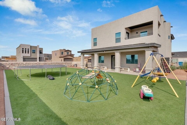 rear view of house with stucco siding, a lawn, a trampoline, a playground, and a balcony