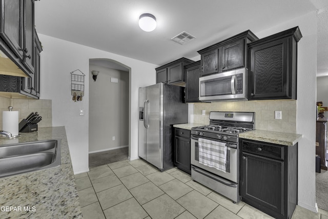 kitchen featuring visible vents, a sink, tasteful backsplash, stainless steel appliances, and arched walkways