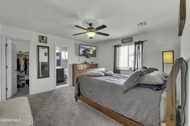 bedroom featuring visible vents, a closet, a textured ceiling, a walk in closet, and light colored carpet